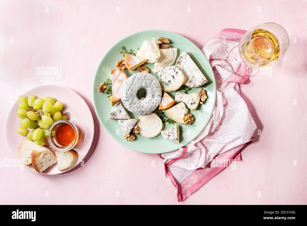 Il piatto di formaggi assortimento di formaggi francesi servite con miele, noci, pane e uva sul turchese piastra in ceramica e vetro di vino bianco su rosa pas Foto Stock