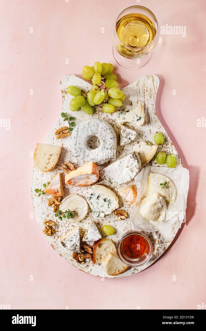 Il piatto di formaggi assortimento di formaggi francesi servite con miele, noci, pane e uva in legno bianco che serve la scheda con un bicchiere di vino bianco su rosa Foto Stock