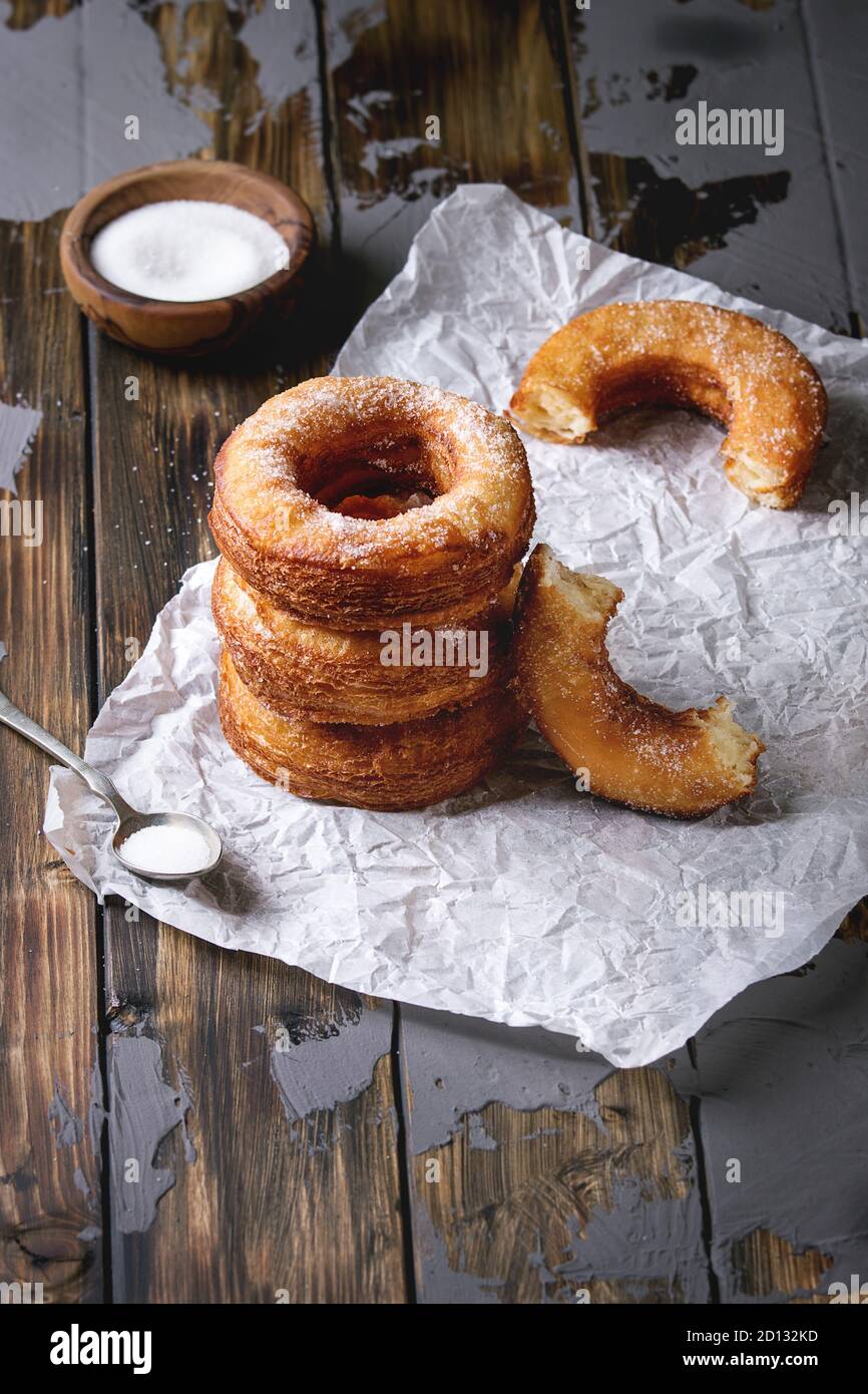 In casa della pasta sfoglia fritti ciambelle o cronuts in stack con zucchero in piedi su carta sgualcita su legno scuro tabella di calcestruzzo. Foto Stock