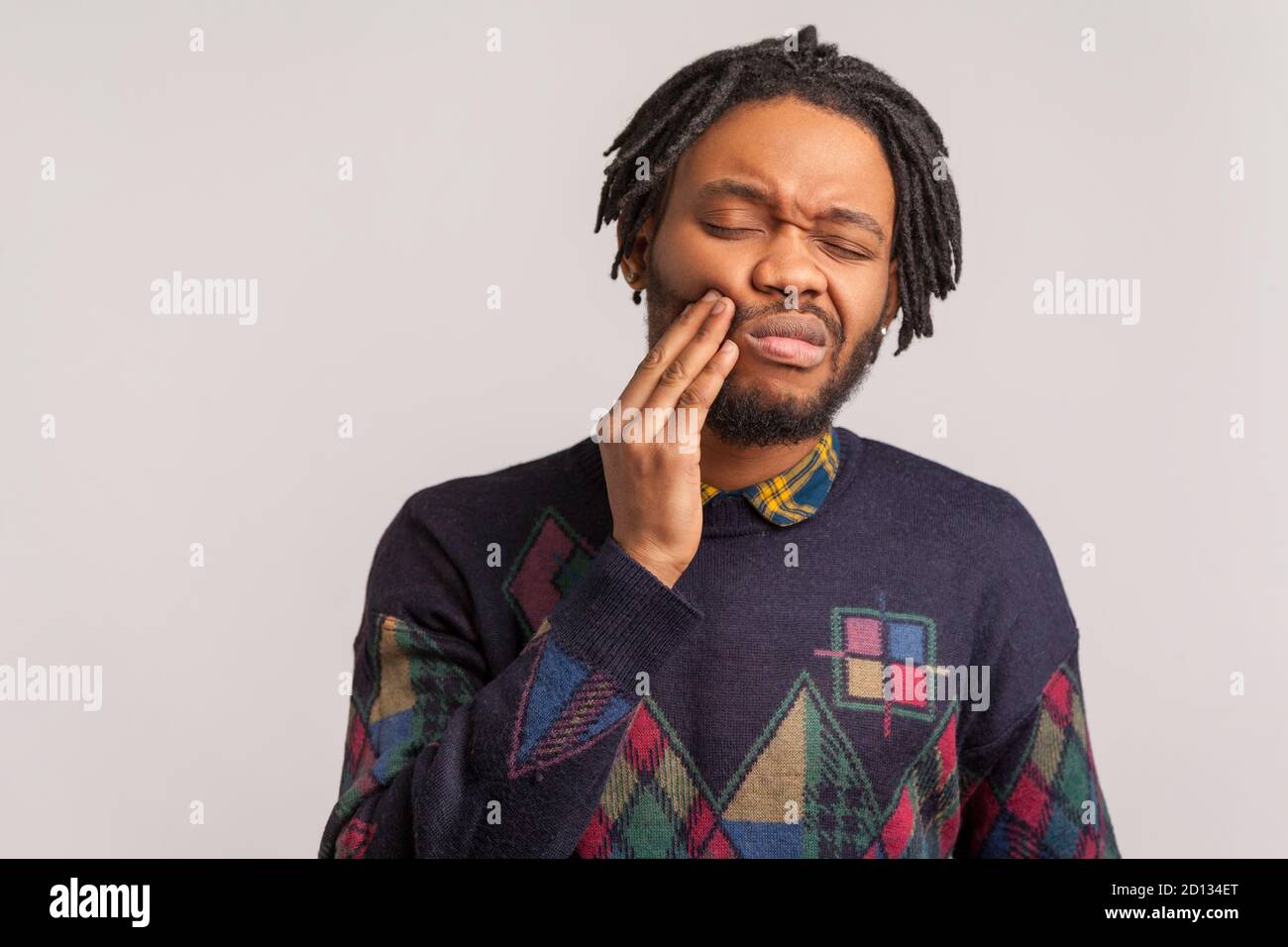 L'uomo afro con barbuto frustrato con i temeblocchi che toccano la guancia e che wincing nel dolore che avverte il dolore terribile dolore del dente, gengivite, malattia parodontale. Interno Foto Stock