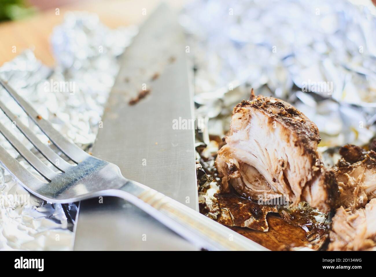 Cibo residuo dopo cena. Primo piano di pezzo di pollo fritto, forchetta sporca e coltello su caffè o tavolo da cucina Foto Stock