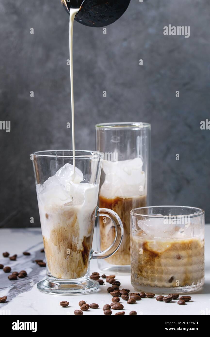 Caffè ghiacciato cocktail o frappe con cubetti di ghiaccio e versare la crema è servita in tre diversi tipi di bicchieri con i chicchi di caffè intorno su marmo bianco tavola con Foto Stock