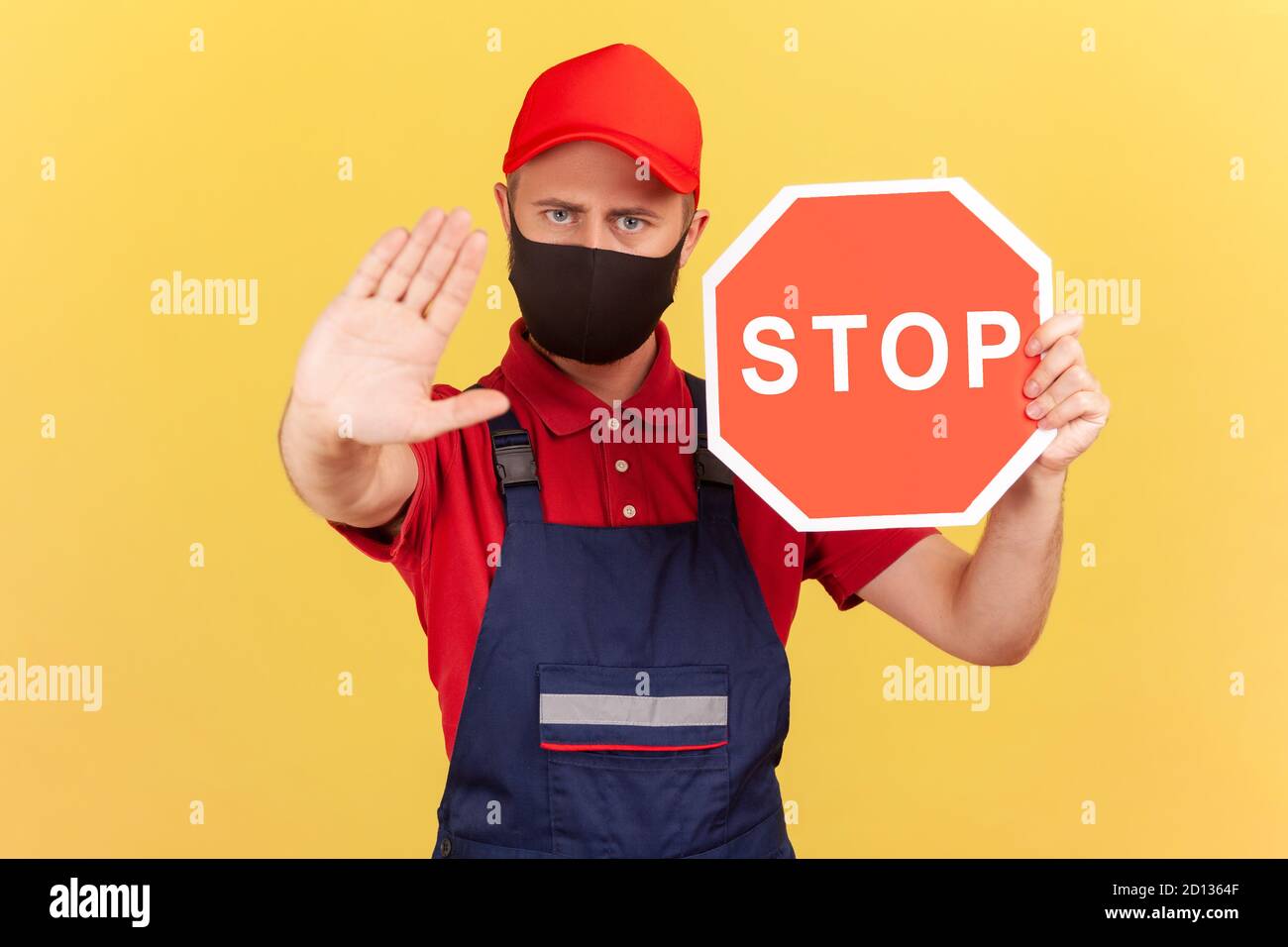 Artigiano in maschera viso uniforme e igienica che mostra il gesto di stop e tenendo il segnale rosso stop, divieti e restrizioni durante la quarantena. Indo Foto Stock