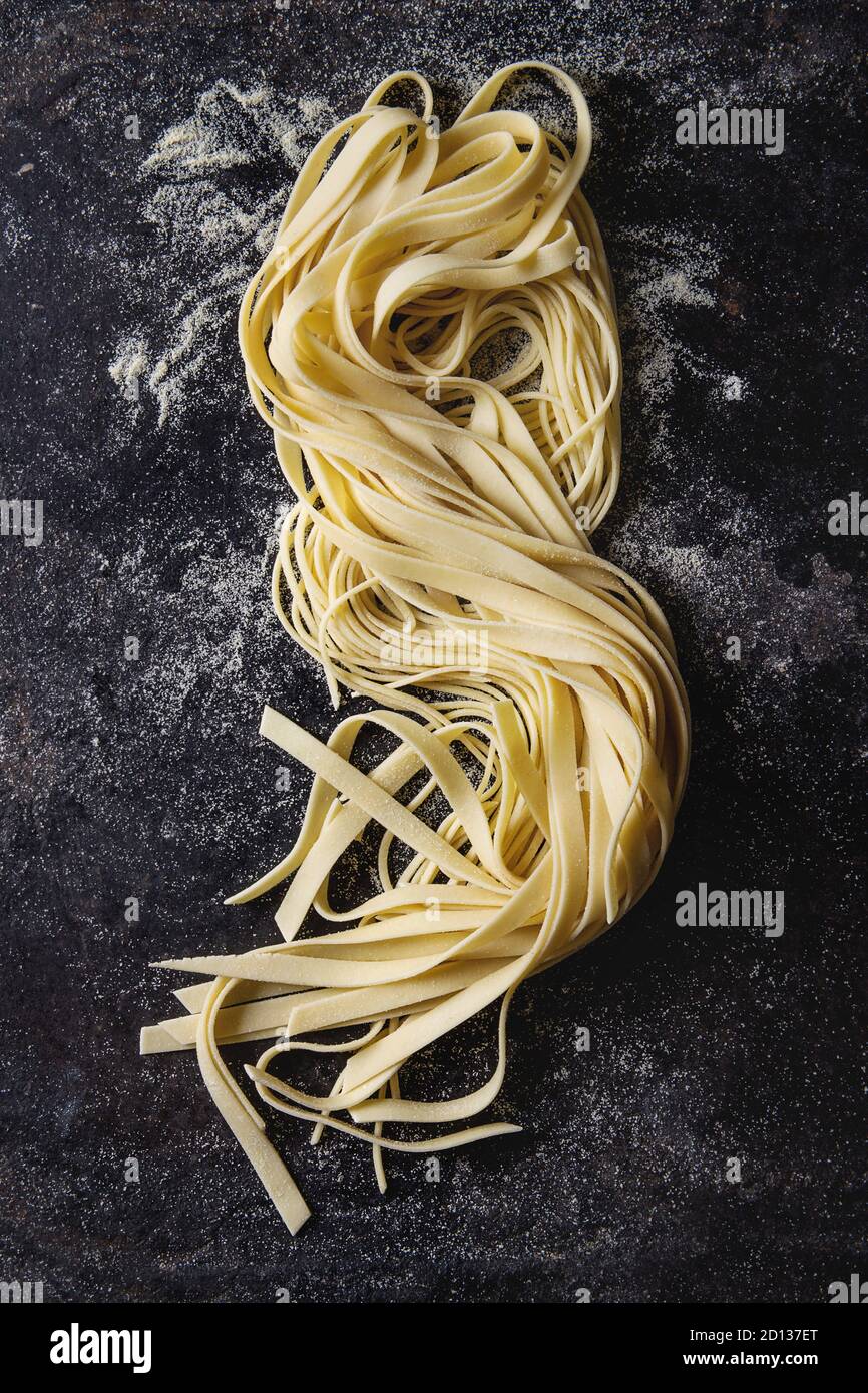 Varietà di artiginale raw pasta cruda spaghetti e tagliatelle con farina di semola su nero sfondo texture. Laici piana, spazio Foto Stock
