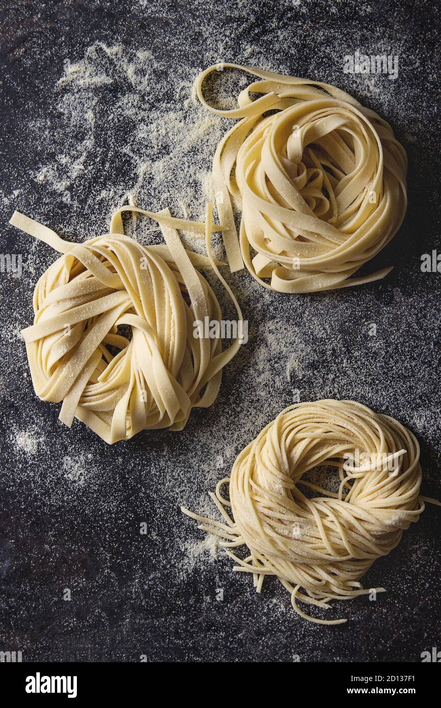 Varietà di artiginale raw pasta cruda spaghetti e tagliatelle con farina di semola su nero sfondo texture. Laici piana, spazio Foto Stock