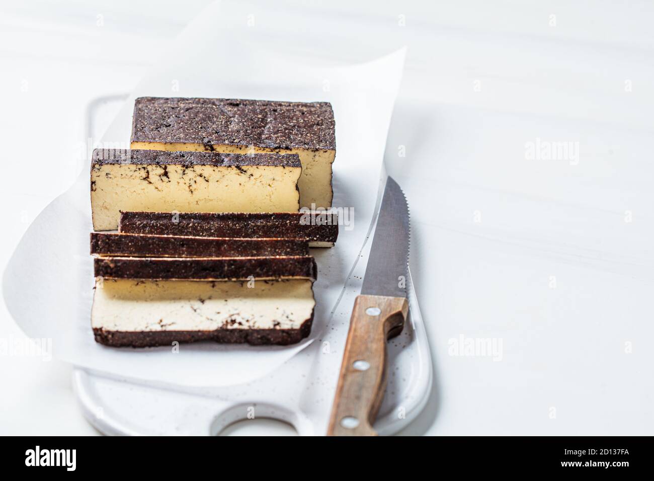 Tofu affumicato a fette su una tavola bianca, sfondo bianco. Concetto di cibo vegano. Foto Stock