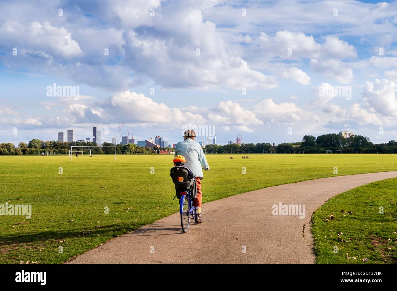 Regno Unito, Londra, Marshes di Hackney. Un ciclista che porta un bambino in un posto di sicurezza su una pista ciclabile in un parco londinese. Sole, giorno d'estate. Foto Stock