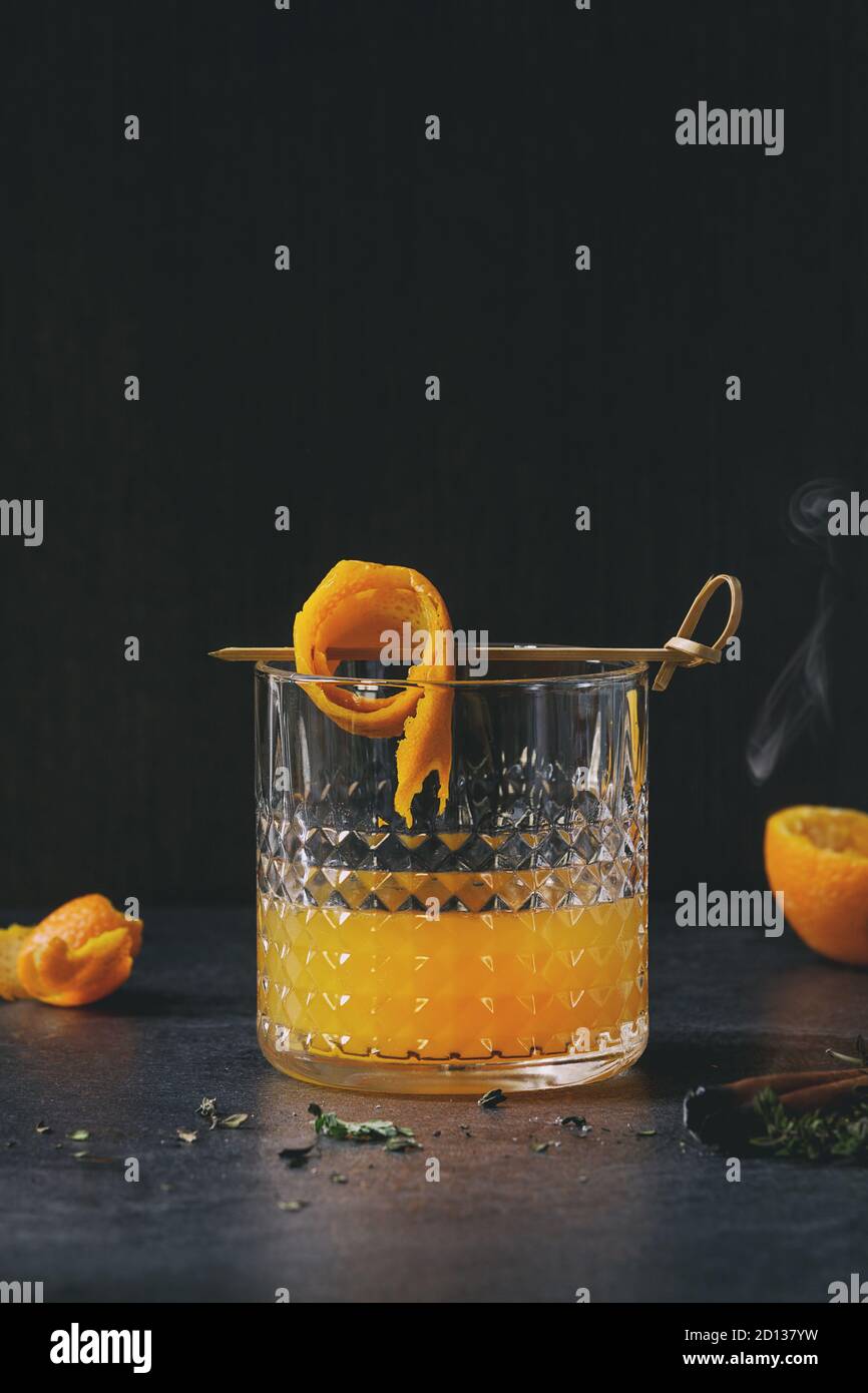 Bicchiere di Scotch whisky succo di arancia cocktail alcolici con roteato a  buccia d'arancia su spiedino, timo e fumare bastoncini di cannella in piedi  sul marmo nero t Foto stock - Alamy