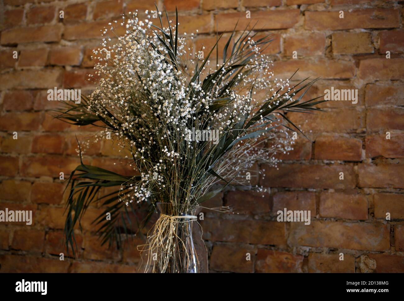 Vaso con piccoli fiori bianchi selvaggi sullo sfondo delle pareti di mattoni, caffetteria, caffetteria, ristorante in stile loft con decorazioni floreali naturali Foto Stock