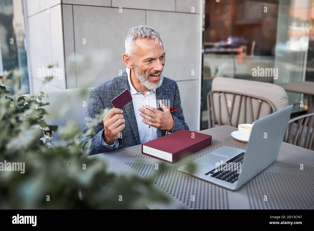 Uomo anziano dai capelli grigi che sorride e mostra una carta di plastica Foto Stock