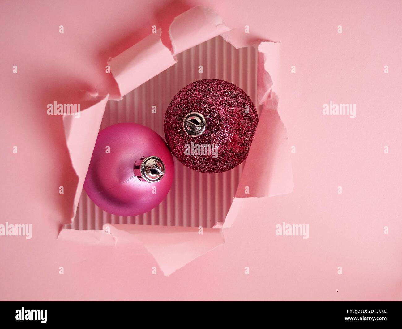 Due palline rosa di Natale in un foro di carta strappato, Natale e concetto di nuovo anno. Foto Stock
