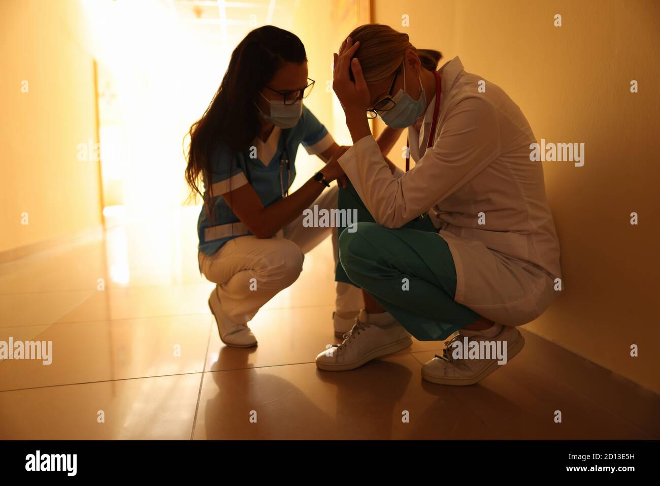 Infermiera calma piangendo medico in uniforme e maschere mediche e. si trova nel corridoio dell'ospedale Foto Stock