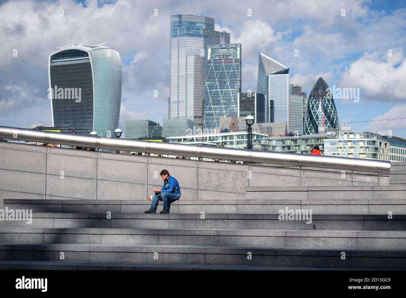 Un uomo si siede e mangia da solo al sole a pranzo vicino al Municipio, nel centro di Londra, dopo che una serie di nuove restrizioni per combattere l'aumento dei casi di coronavirus è entrato in vigore in Inghilterra. Foto Stock