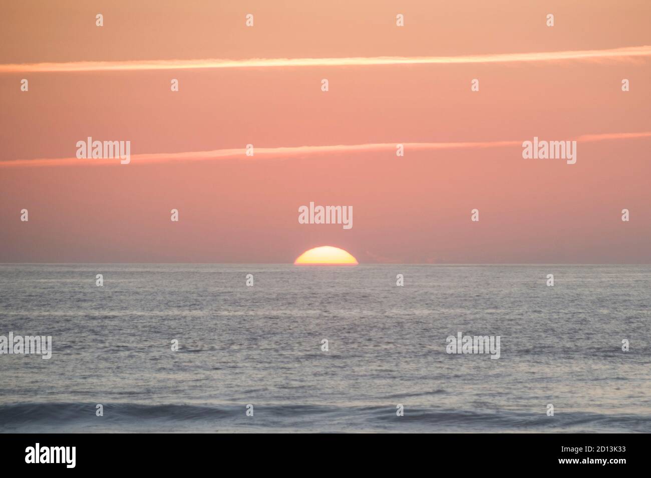 Grande sole che tramonta sull'oceano, quasi scomparendo la linea dell'orizzonte, con una calda e forte tonalità arancione Foto Stock