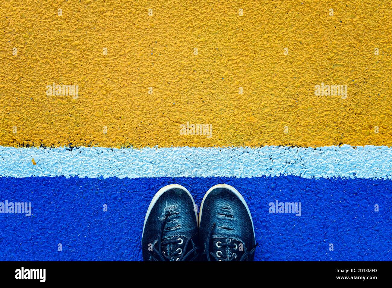 Vista dall'alto delle gambe femminili in piedi accanto alla linea bianca su sfondo blu. Concetto di separazione Foto Stock