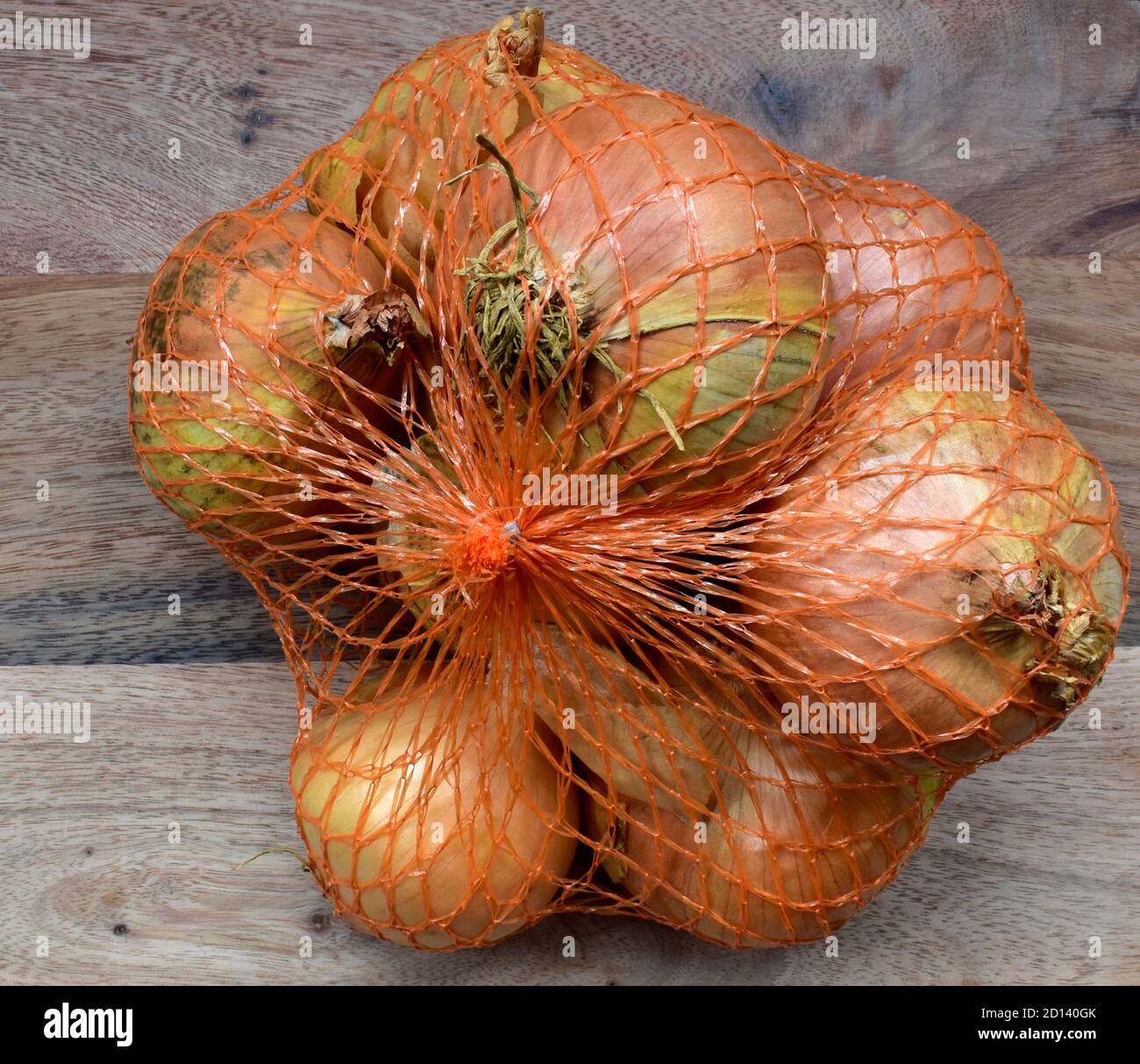 Cipolle da cucina bianche in sacchetto di plastica per rete dal fornitore di Norfolk UK su un tagliere di legno. Foto Stock