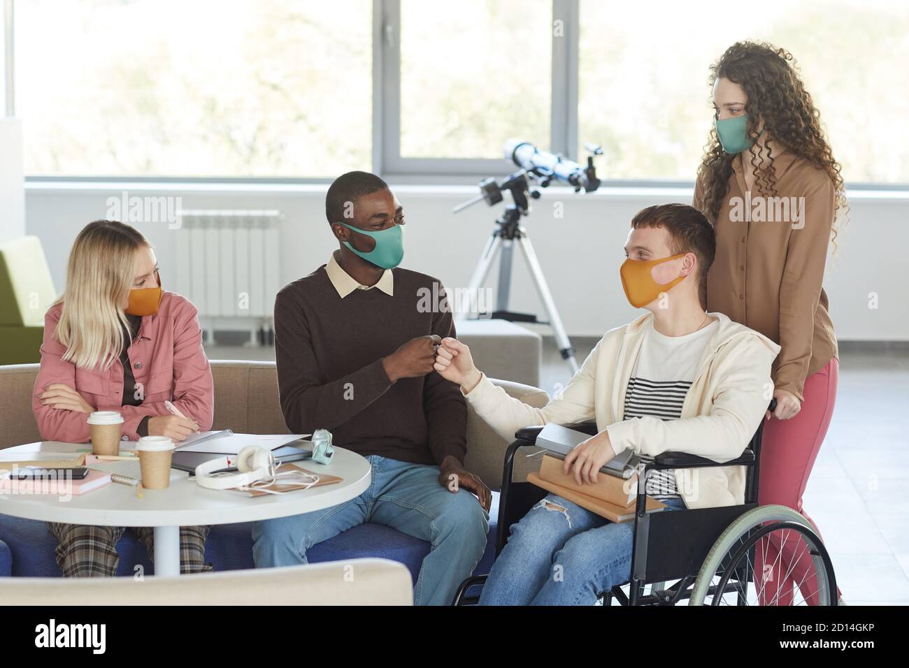 Ritratto di un gruppo multietnico di studenti che indossano maschere mentre studiano in biblioteca universitaria con un giovane uomo che usa la sedia a rotelle in primo piano, copy space Foto Stock