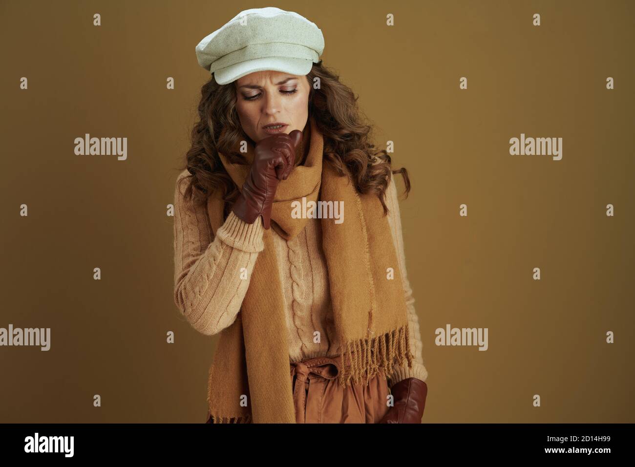 Ciao settembre. Casalinga moderna di mezza età in sciarpa con guanti in pelle tosse isolato su sfondo marrone. Foto Stock