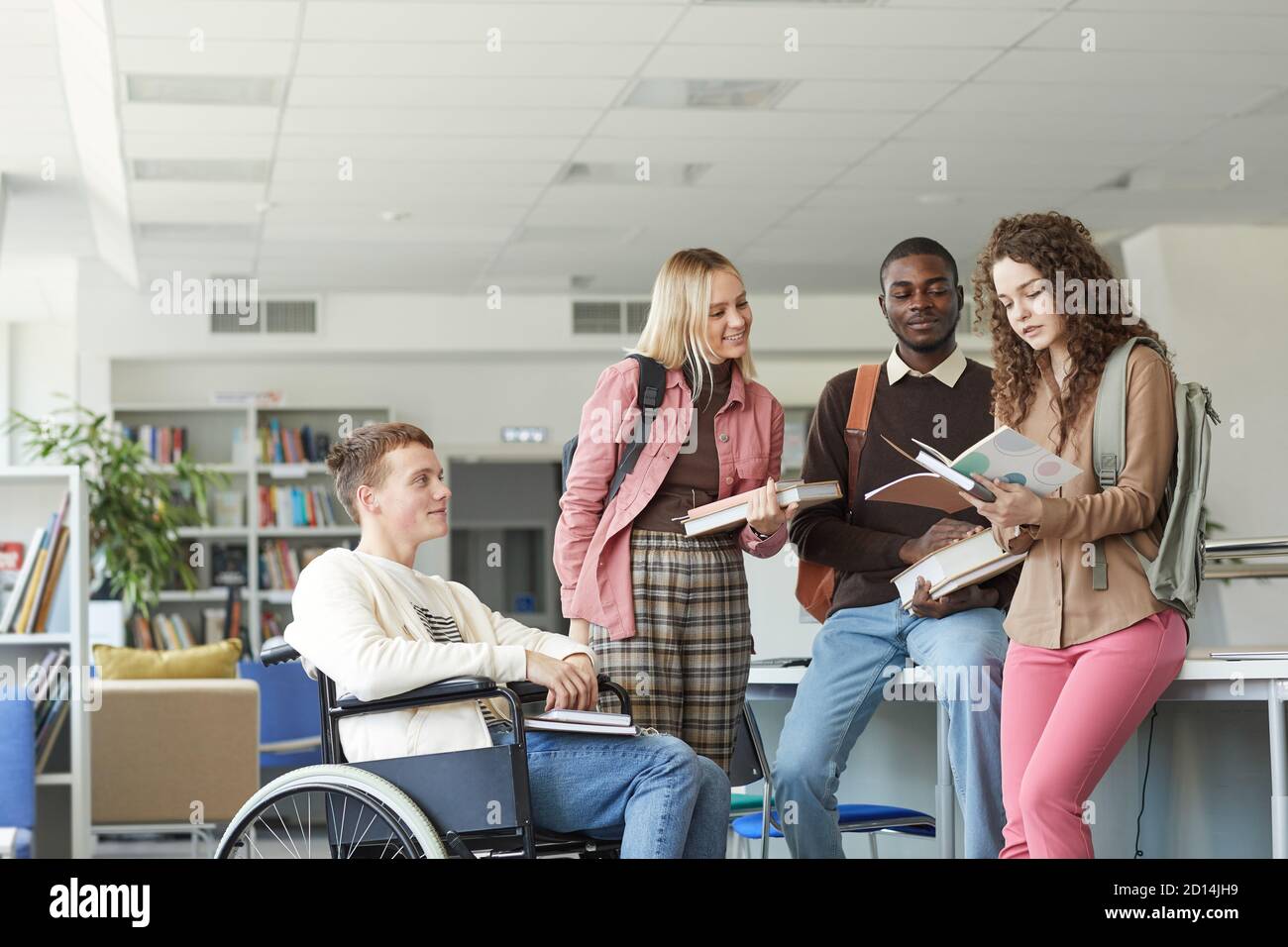 Ritratto di un gruppo multietnico di studenti nella biblioteca universitaria con il ragazzo in sedia a rotelle in primo piano, spazio di copia Foto Stock