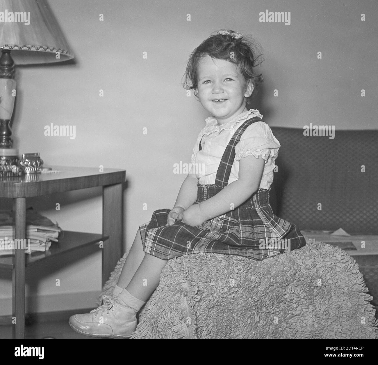 Stile di vita degli anni '50 d'epoca, la ragazza di due anni pone per la macchina fotografica nel suo ponticello della Plaid, Stati Uniti Foto Stock