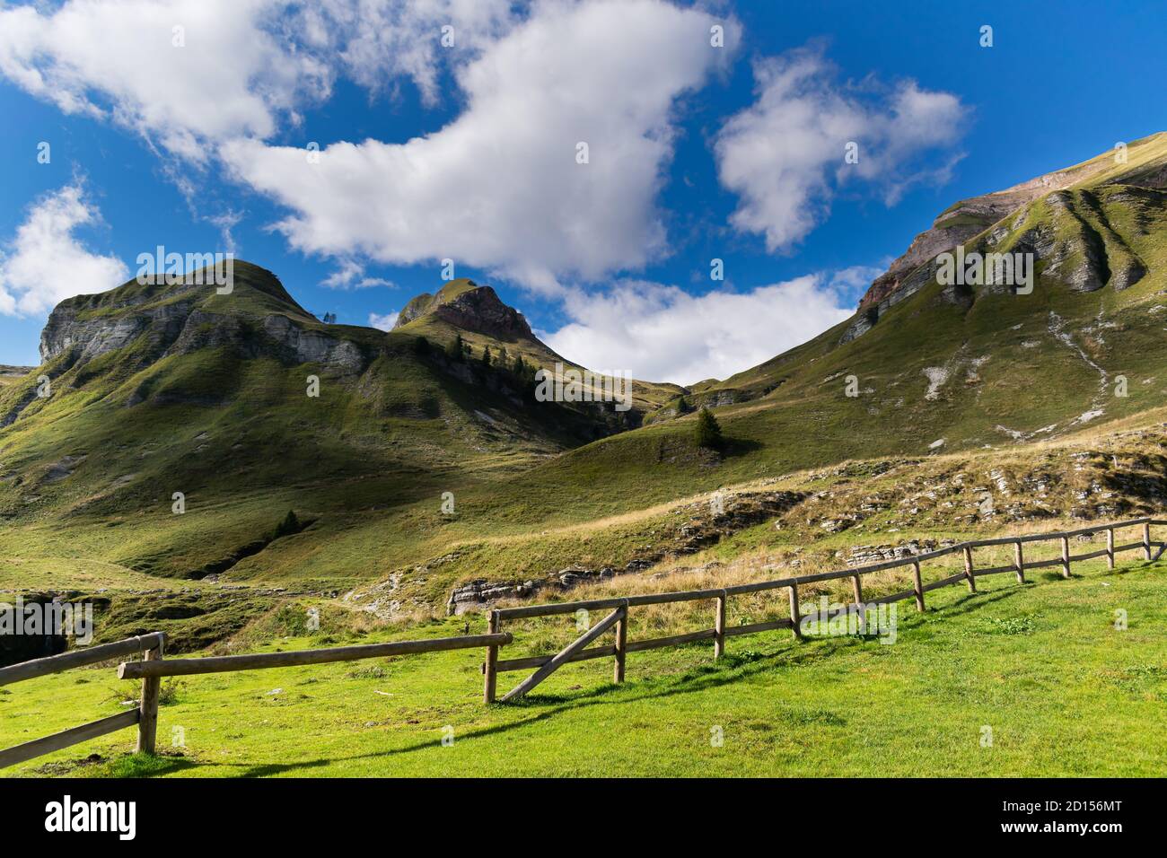 Suggestivo paesaggio montano, cielo blu con nuvole bianche, verdi pendii con una recinzione in legno che confina con il cottage del pastore. Piani eterni, Dolomiti Foto Stock