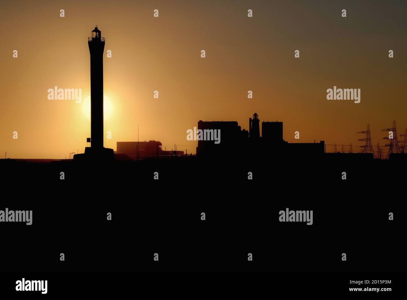 Mentre il sole affonda dietro il faro di 43 m (141 piedi) che ha allertato la navigazione della Manica navigando nello stretto di dover al pericolo del promontorio di Dungeness che si aggirava nel mare sin dalla sua apertura nel 1961, sembra naufrare un precedente faro edoardiano, aperto nel 1904, che usava una lampada in paraffina. A distanza si trovano anche i reattori e la sala turbine di Dungeness A, una centrale nucleare di Magnox che ha generato elettricità dal 1965 al 2006, dopo di che è stata smantellata in modo sicuro. Foto Stock