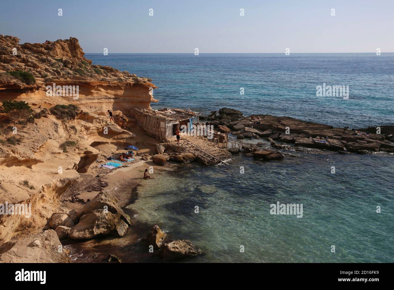 Spagna, Isole Baleari, formentera, calo des mort, visitatori estivi adagiati su una baia fiancheggiata da scogliere rosse e rocce in un forte di acque turchesi Foto Stock