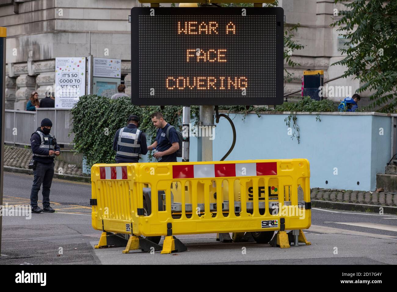 Un uomo viene avvertito accanto a un cartello di avvertenza "indossare una copertura facciale" che indica ai pendolari di indossare una maschera facciale sui trasporti pubblici, Waterloo Station, Regno Unito Foto Stock