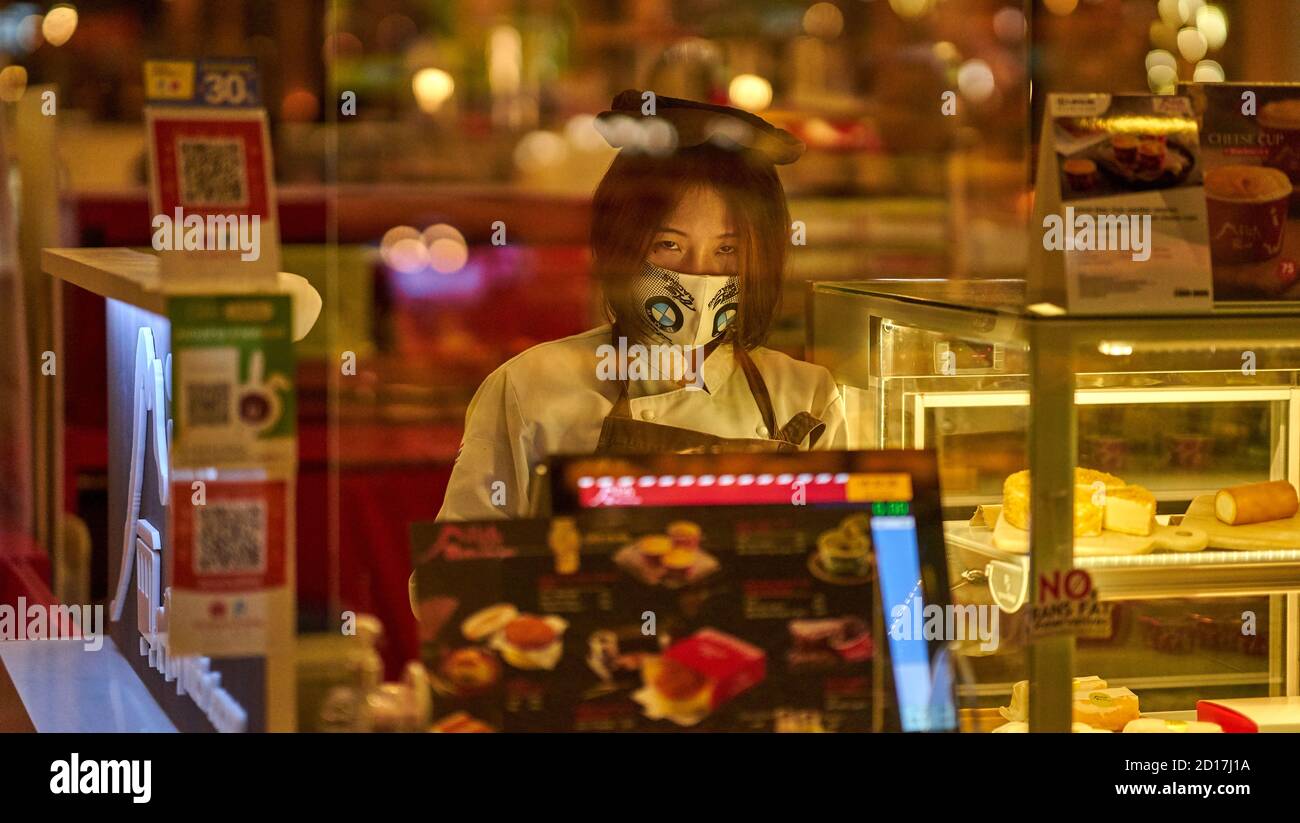 Un assistente di negozio femminile che indossa una maschera protettiva per il viso. Foto Stock