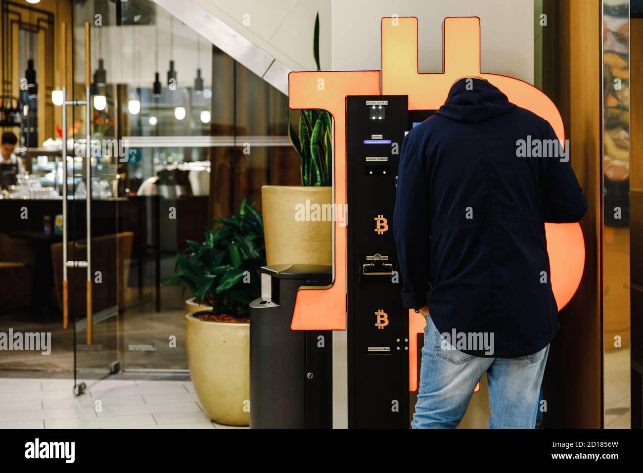 Riga, Lettonia - circa Ottobre, 2020: Uomo calvo utilizza Bitcoin ATM macchina in centro commerciale per lo scambio di criptovaluta Foto Stock