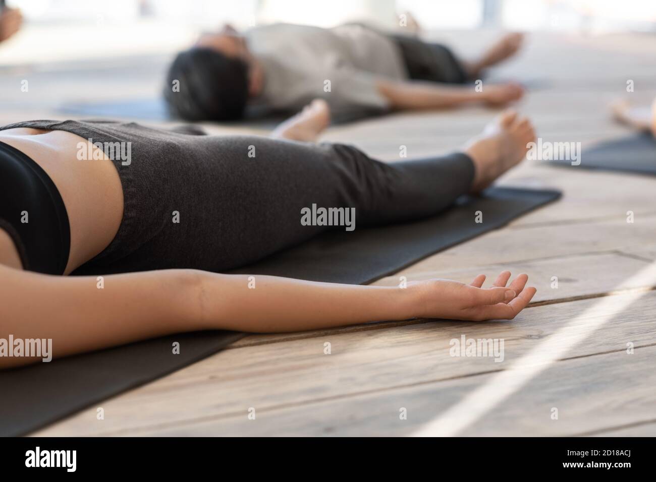 Donna irriconoscibile sdraiata sul tappetino in posa cadavere, praticando yoga in studio Foto Stock