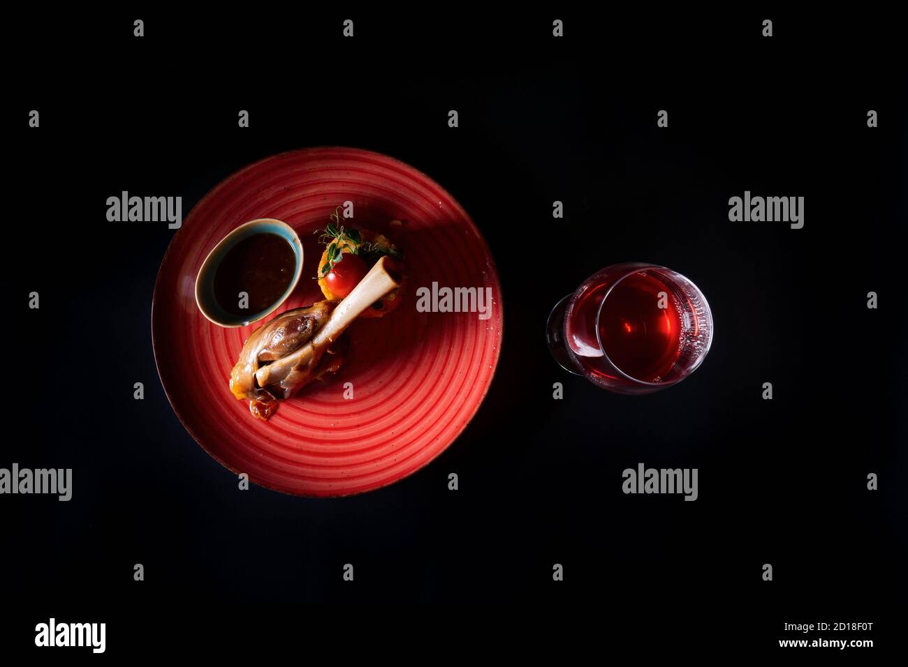 Gamba di agnello con salsa su un piatto rosso e un bicchiere di vino su sfondo nero Foto Stock