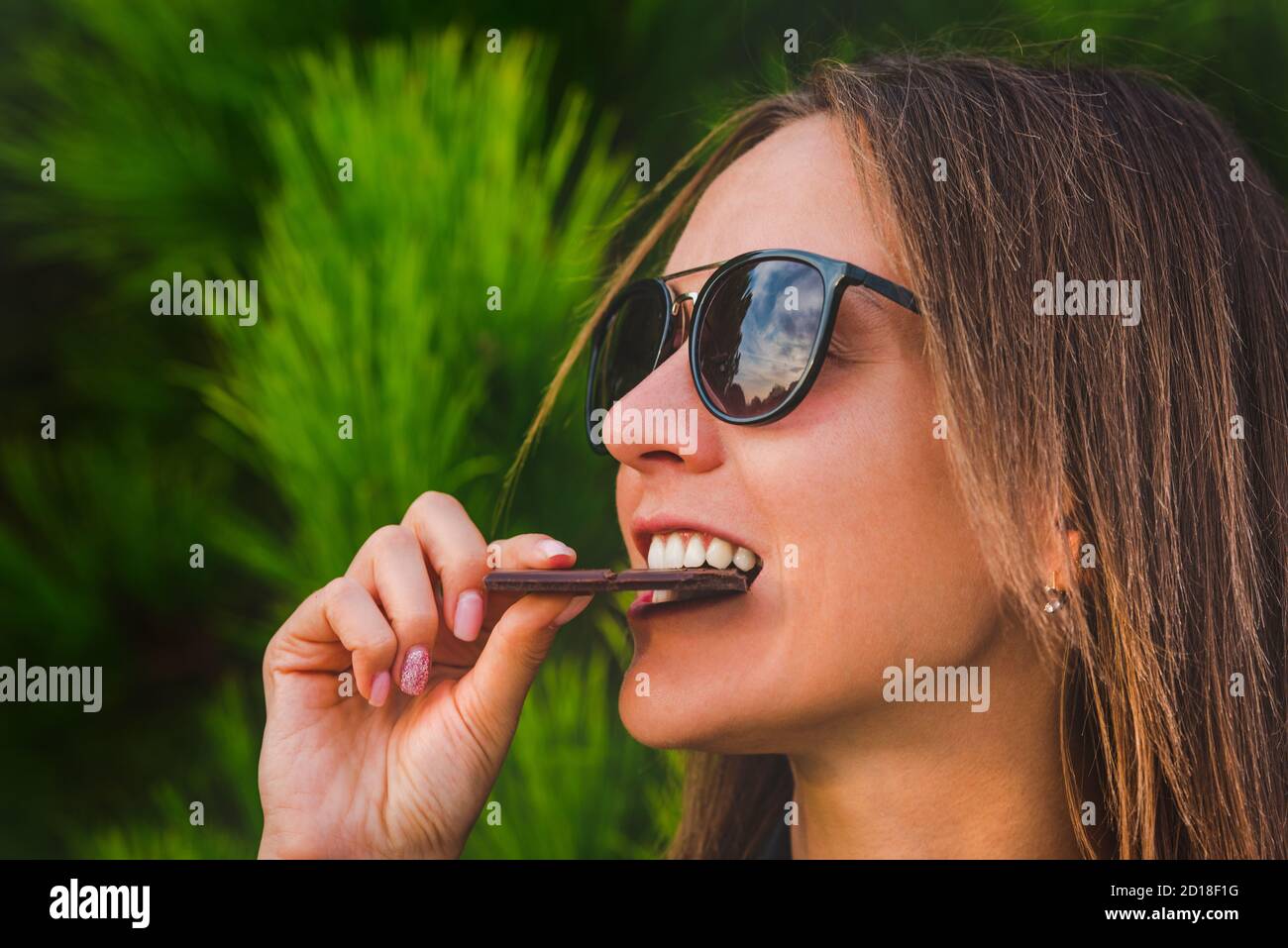 Carina giovane femmina mangiare cioccolato bar. Primo piano di donna faccia mordere cioccolato fondente. Foto Stock