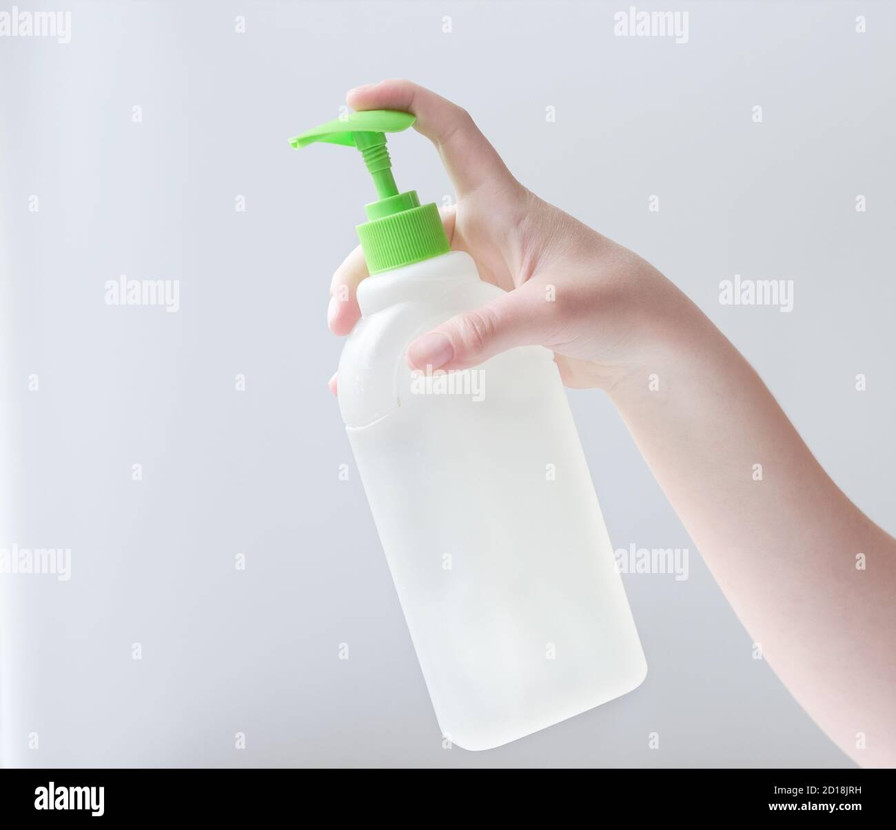La mano della giovane donna tiene il detersivo bianco della bottiglia del sanitaizer per le superfici differenti in cucina, in bagno e in altre stanze. Primo piano. Sfondo grigio chiaro. Concetto di pulizia del bagno Foto Stock