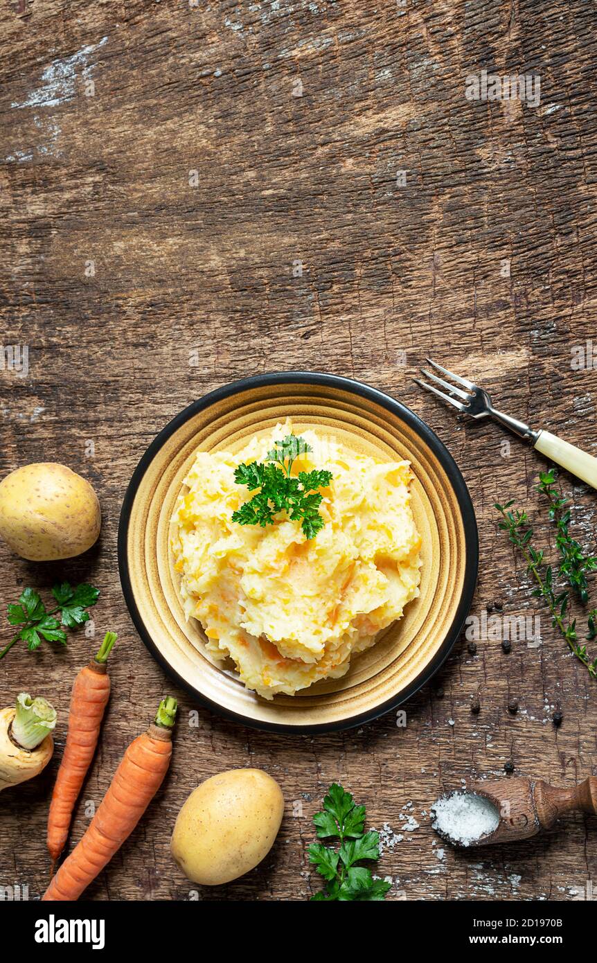 Purè di pastinaca con patate e carote e ingredienti per preparare gustose purè di pastinaca su sfondo di legno scuro. Vegetariano sano e delizioso Foto Stock