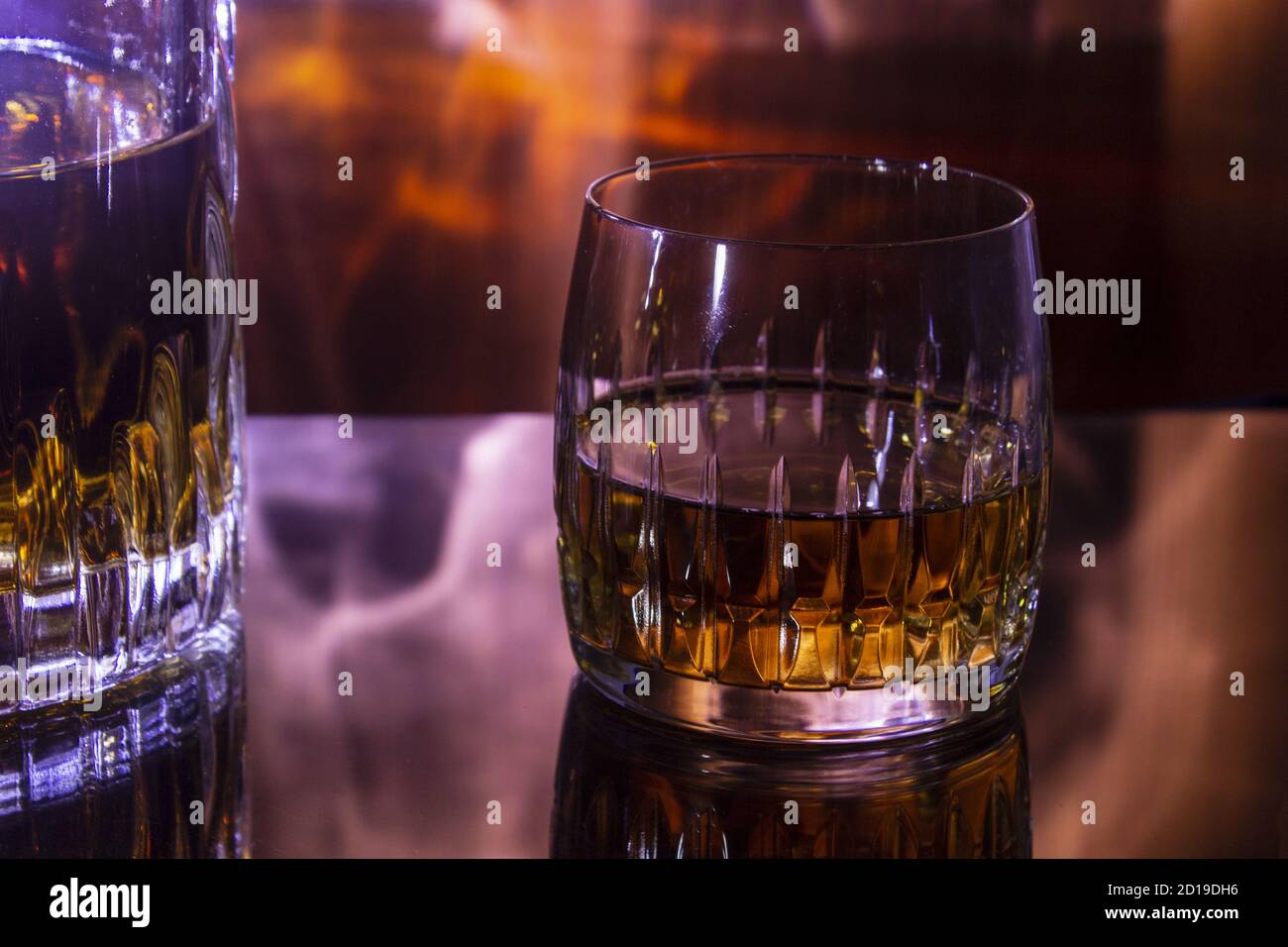 Decanter e bicchiere di whiskey su un sfondo Fiery. Decanter e vetro sono in mirroring su un tavolo di vetro. Foto Stock