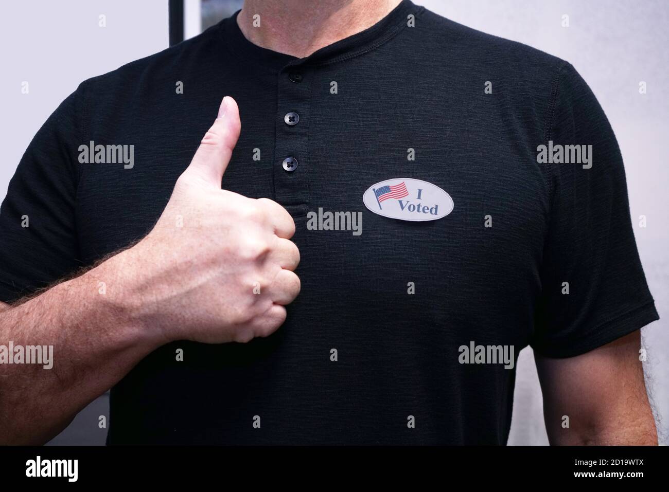 Primo piano torso dell'uomo in camicia nera indossando ho votato adesivo dando un pollice dopo la votazione. Foto Stock