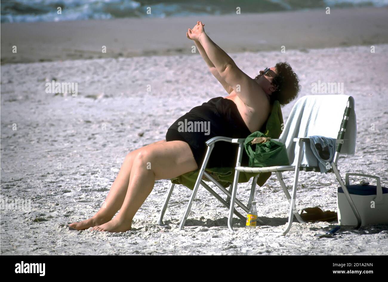 La donna sovrappeso fa gli esercizi di striching mentre si siede in una sedia sulla spiaggia Foto Stock