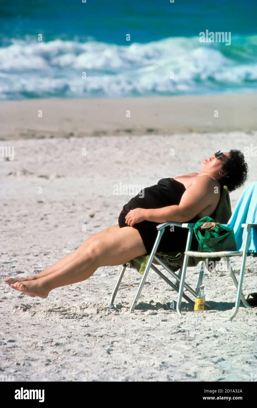 La donna sovrappeso fa gli esercizi di striching mentre si siede in una sedia sulla spiaggia Foto Stock