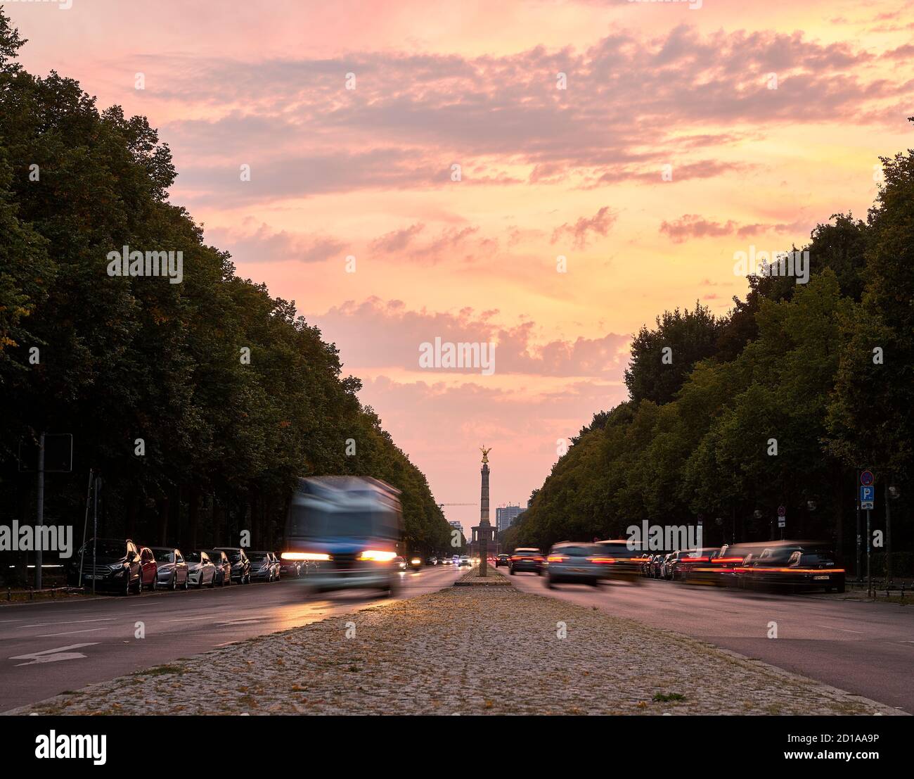 Attraversa il Tiergarten Park con auto sfocate in movimento e. Colonna della Vittoria di Berlino (Siegessäule) sullo sfondo durante il tramonto Berlino Foto Stock