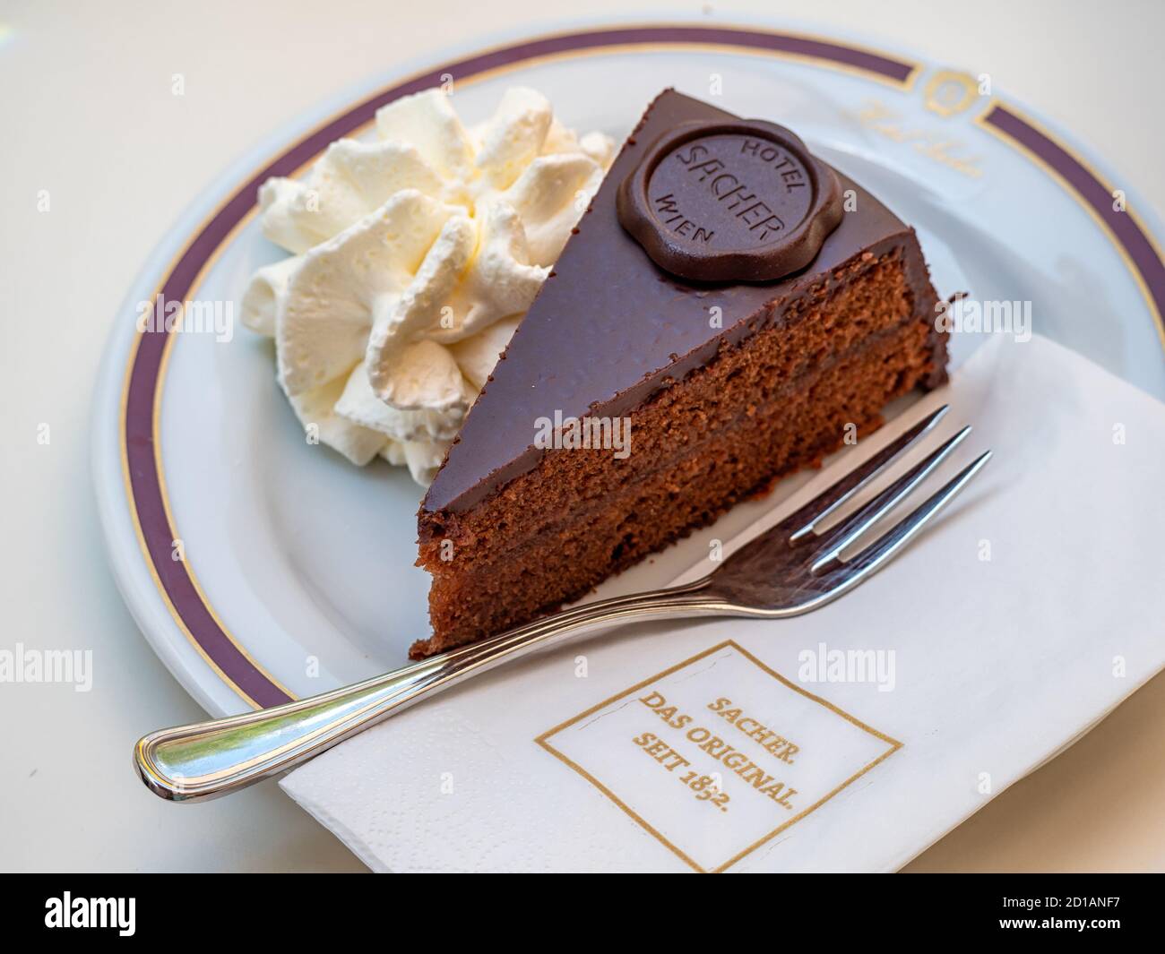VIENNA, AUSTRIA - 14 LUGLIO 2019: Fetta di torta Sacher-torta sul piatto al Cafe Sacher con tovagliolo e forchetta di marca Foto Stock