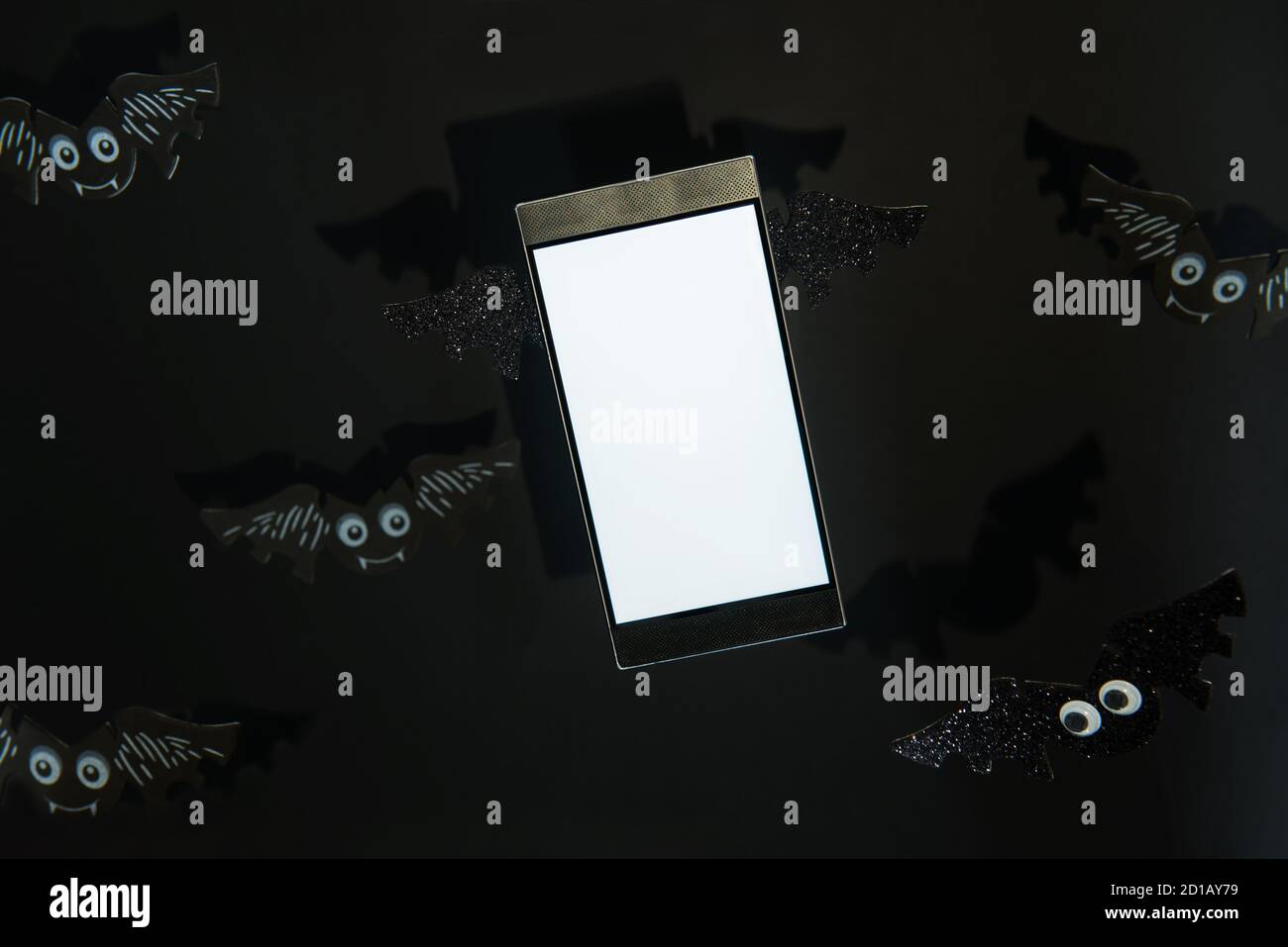 Primo piano smartphone volante con schermo bianco vuoto decorato con ali a forma di pipistrello sullo sfondo nero con pipistrelli. Immagine con ombre dure. Hallow Foto Stock