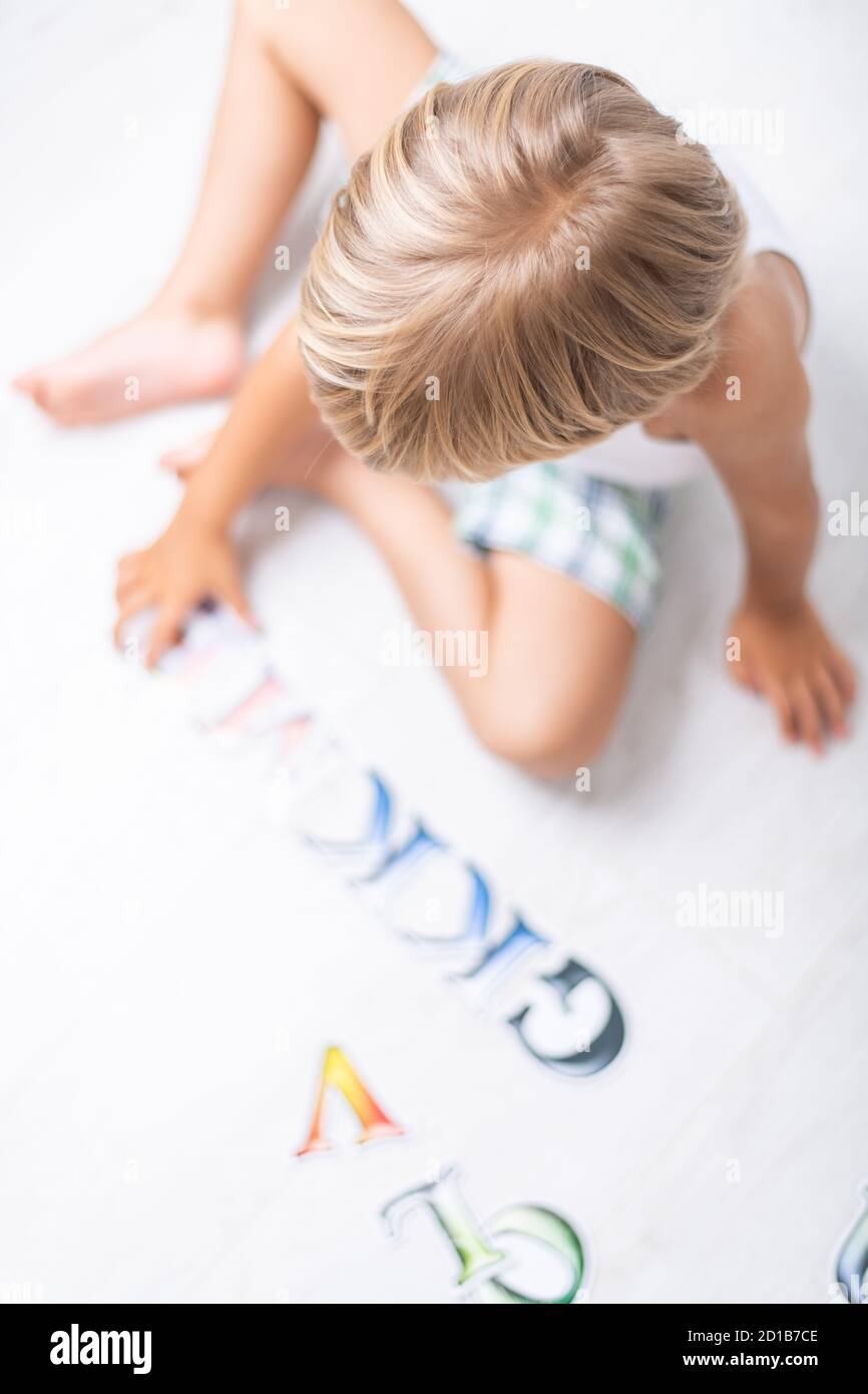 Bel ragazzo imparando lettere sul pavimento a casa. Vista dall'alto. Foto Stock