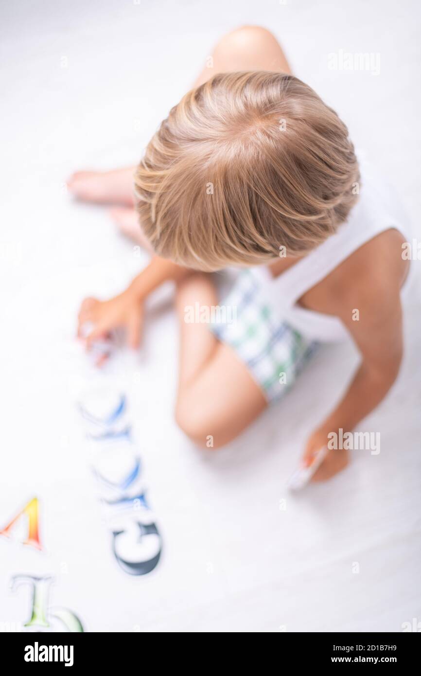 Bel ragazzo imparando lettere sul pavimento a casa. Vista dall'alto. Foto Stock