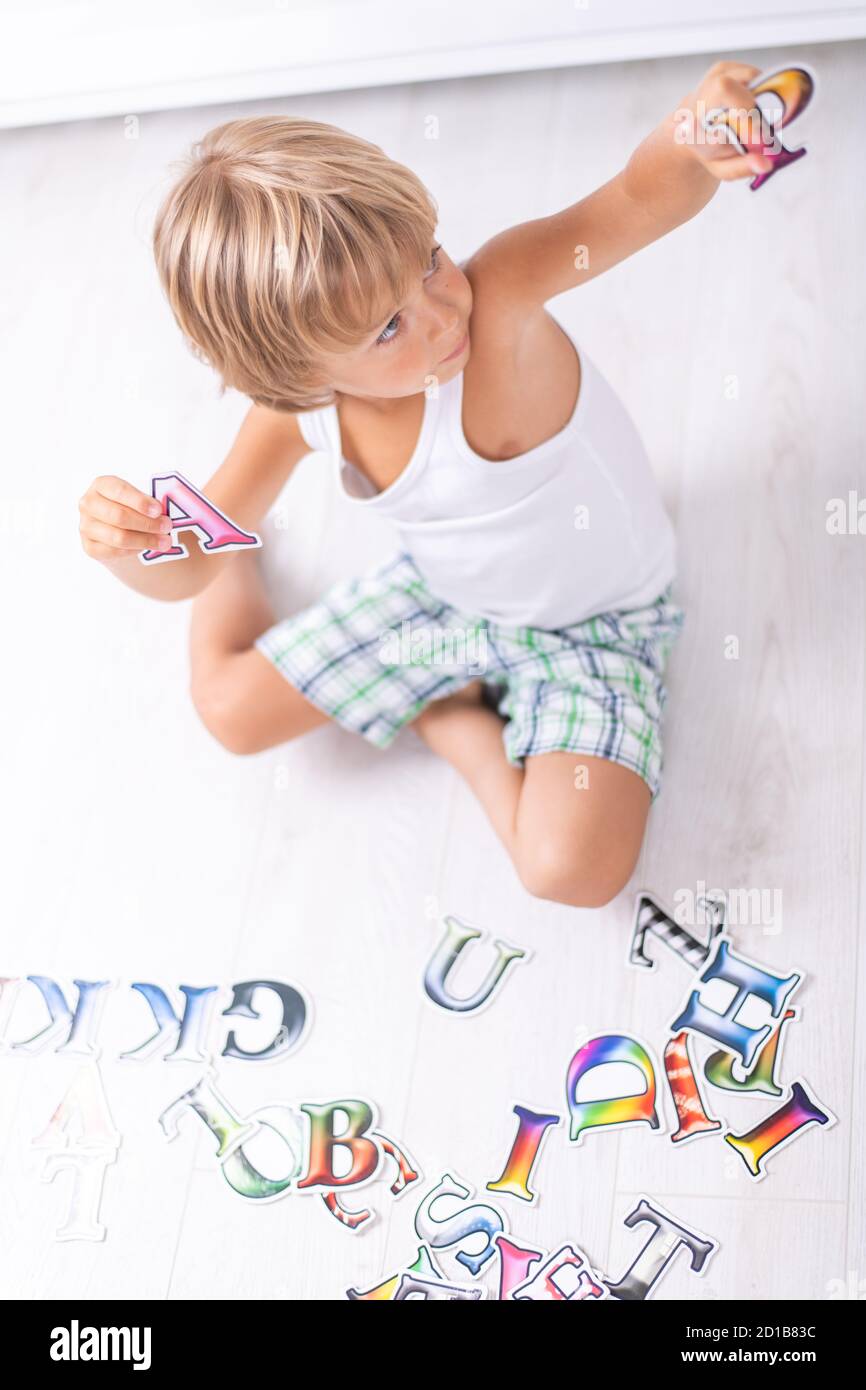 Bel ragazzo imparando lettere sul pavimento a casa. Vista dall'alto. Foto Stock