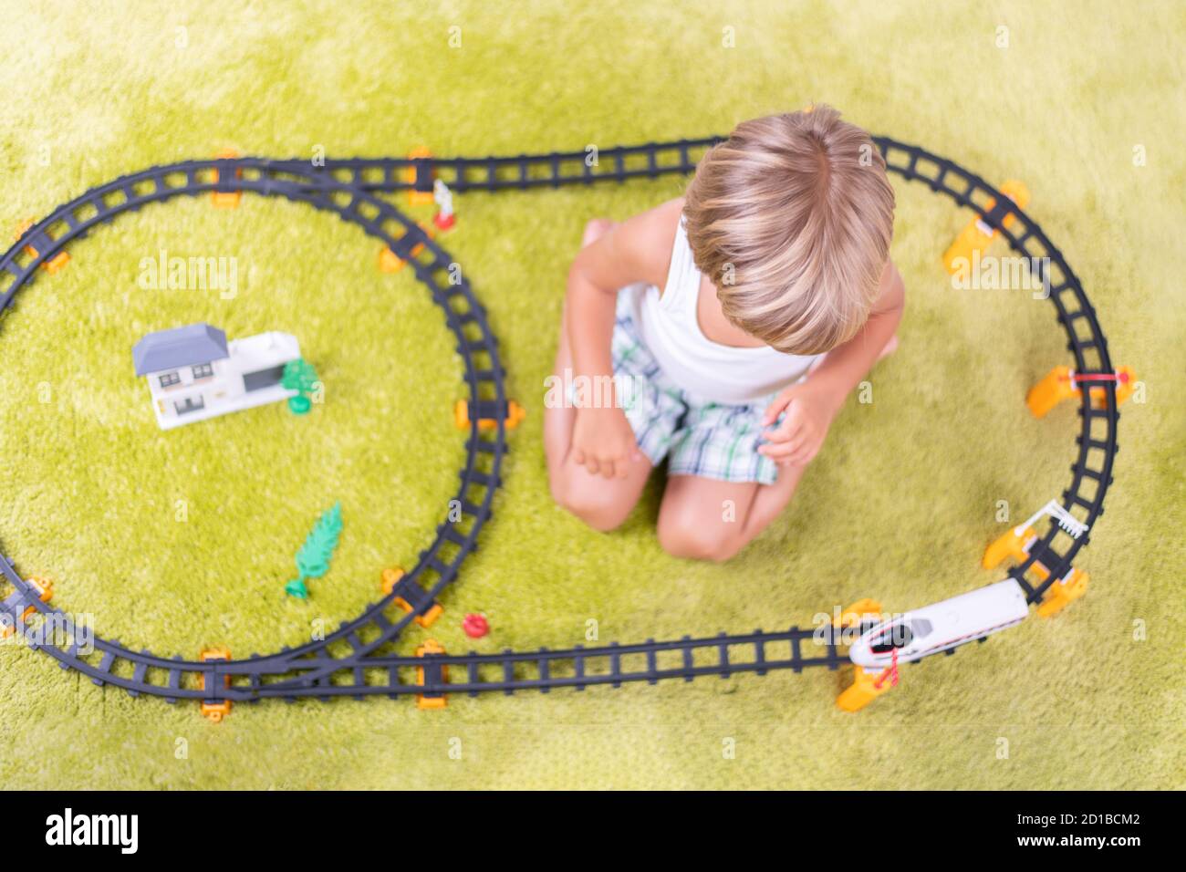 Il ragazzo gioca con la ferrovia di plastica. Bambino con treno giocattolo. Giocattoli didattici per bambini piccoli. Ragazzino che costruisce binari ferroviari su tappeto verde. Foto Stock