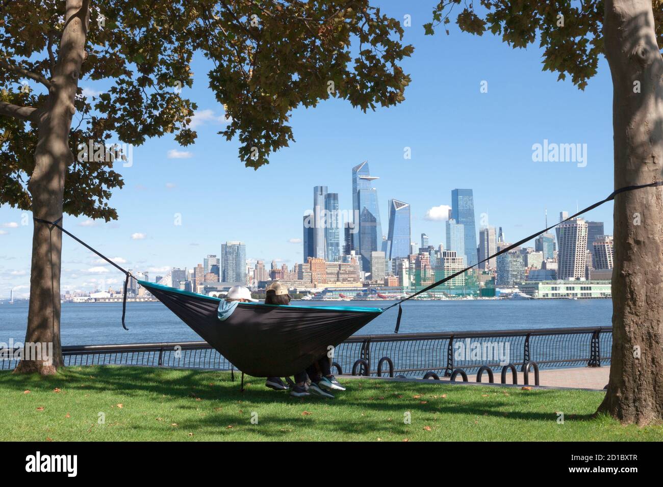 Coppia in amaca godendo della vista dello skyline di New York/Manhattan dall'altra parte del fiume Hudson a Hoboken, il lungomare del New Jersey. Foto Stock