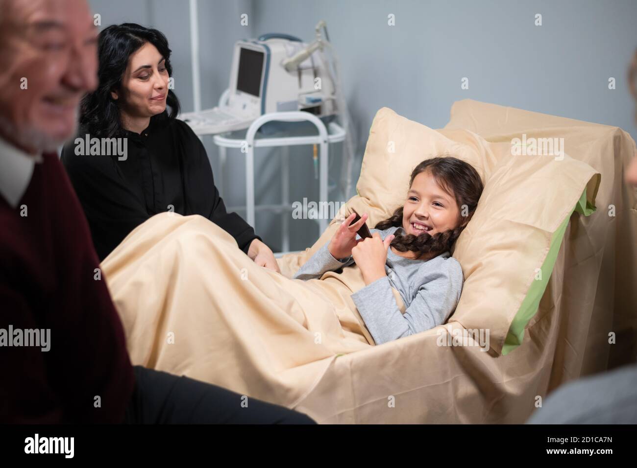 Una famiglia che visita una bella, bambina dopo un incidente, la ragazza è sdraiata a letto in un reparto di ospedale. Foto Stock