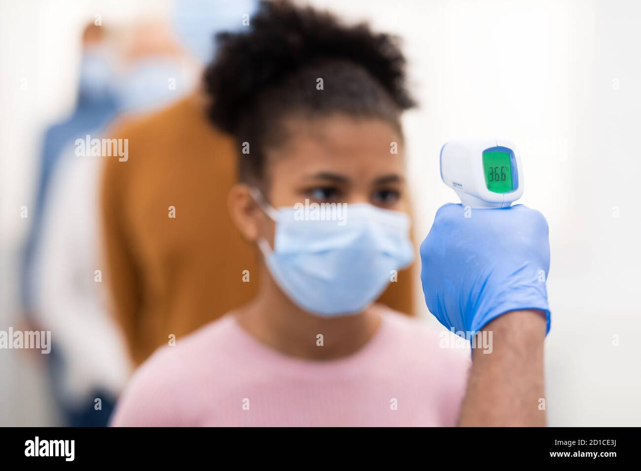 Lavoratore medico che esegue lo screening della temperatura per le persone in coda in interni Foto Stock