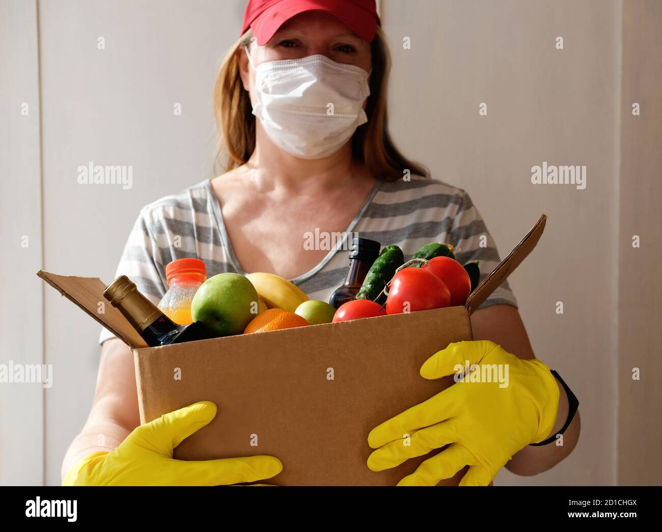 Shopping sicuro in pandemic. Donna Courier indossare maschera facciale, guanti che consegna ordine di drogheria in epidemia di coronavirus. Fornitura di cibo durante l'epidemia di corona virus. Pasto da asporto. Cibo di scorta della gente. Foto Stock